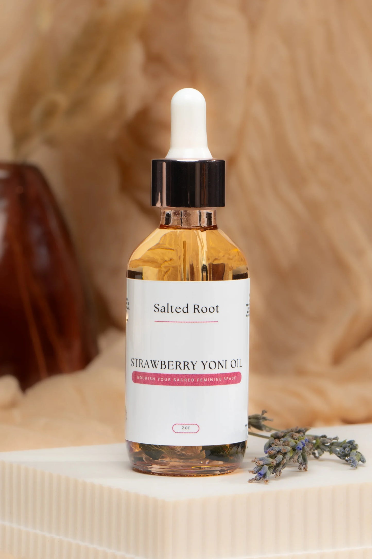 Bottle of Salted Root Strawberry Yoni Oil with a dropper on a textured surface.