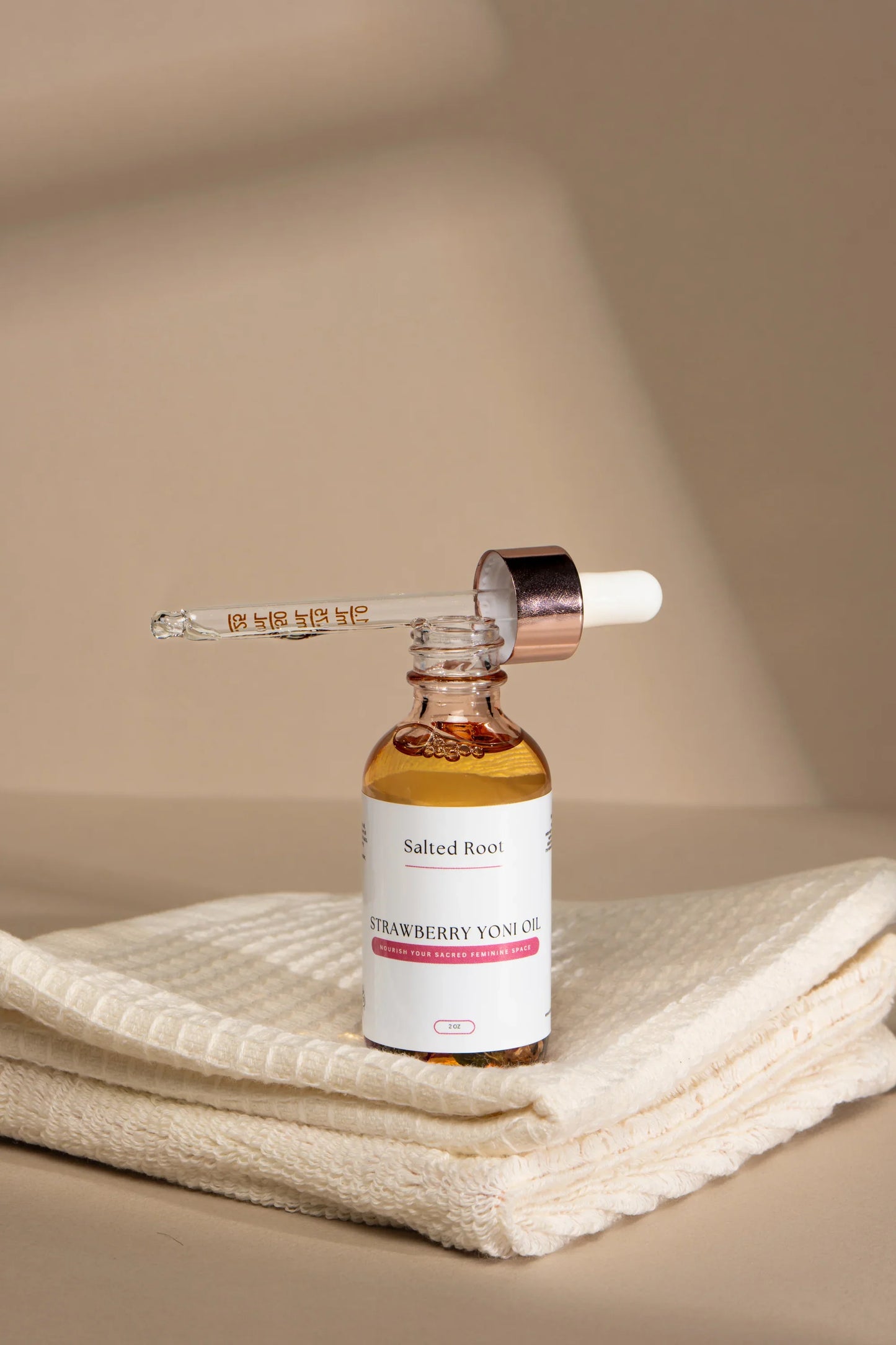 Strawberry Yoni Oil bottle with dropper on a beige towel against a beige background