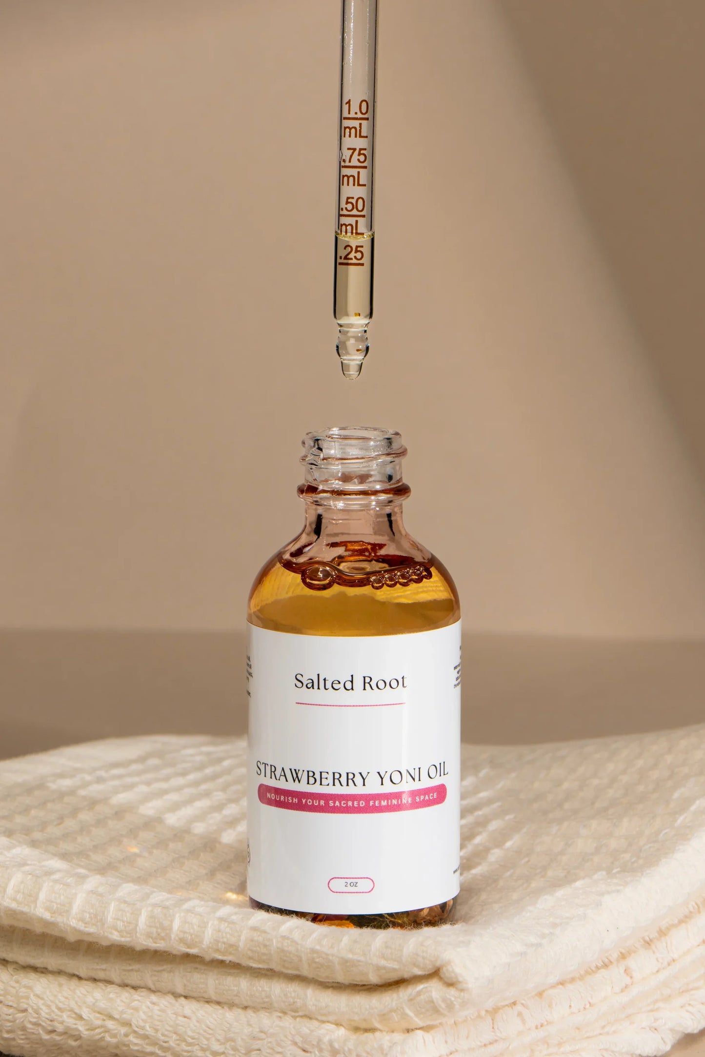 Bottle of 'Salted Root' Strawberry Yoni Oil with a dropper on a beige surface.