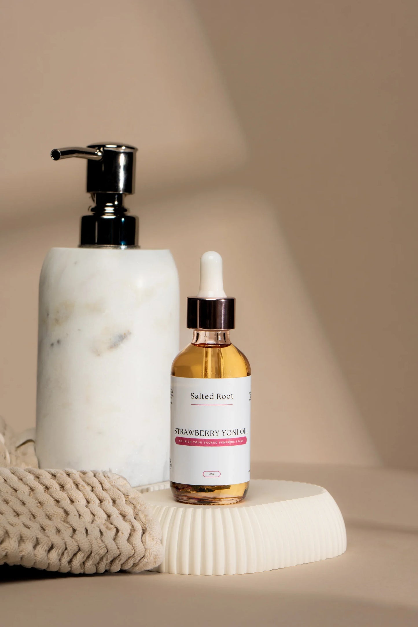 White marble dispenser and Strawberry Yoni Oil on a beige surface with soft lighting.